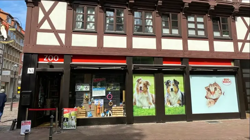 Front Ansicht der Zoo-Busch Filiale in der Innenstadt. Ein altes Fachwerkhaus mit vielen Fenstern. 2 Enten laufen von rechts nach links.